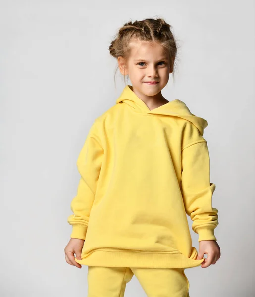 Schattig gehoorzaam voorschoolse meisje, bescheiden poseren op een lichte achtergrond in een gele hoodie met een kap. — Stockfoto