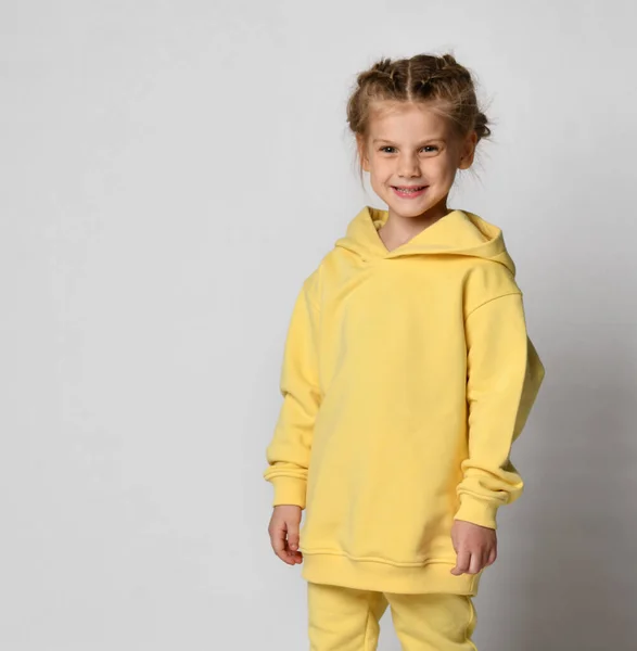 Studio portret van een klein schattig meisje in een warm geel sportpak op een witte achtergrond. — Stockfoto