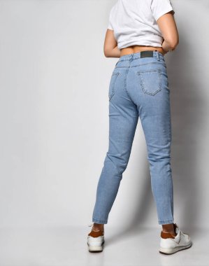 Genç, sıska, şık kot pantolon ve beyaz spor ayakkabılar giymiş bir kadın..