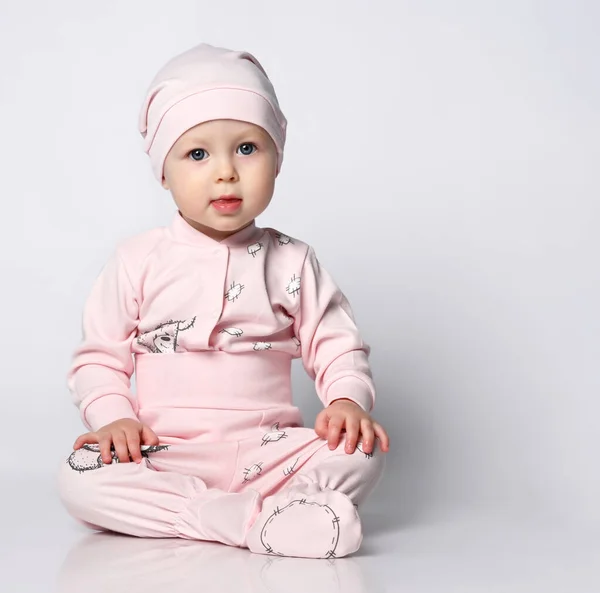 Baby infant in a body with long sleeves and a shianishka, a matching hat, with a funny childish pattern on his clothes, sits on the floor in the studio. — Stock Photo, Image