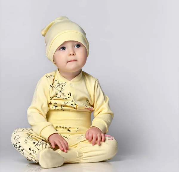 Bebê bebê em um corpo com mangas compridas e um shianishka, um chapéu correspondente, com um padrão infantil engraçado em suas roupas, senta-se no chão no estúdio. — Fotografia de Stock