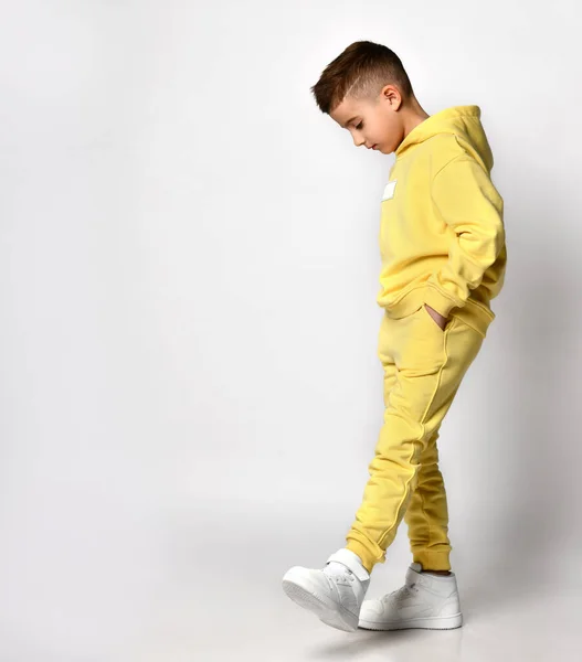 Profilansicht eines kleinen brünetten Jungen in gelber Sportbekleidung und weißen Turnschuhen. — Stockfoto