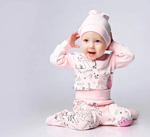Bebê bebê em um corpo com mangas compridas e um shianishka, um chapéu correspondente, com um padrão infantil engraçado em suas roupas, senta-se no chão no estúdio. — Fotografia de Stock
