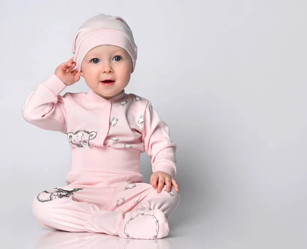 Bebé infante en un cuerpo con mangas largas y un shianishka, un sombrero a juego, con un patrón infantil divertido en su ropa, se sienta en el suelo en el estudio. — Foto de Stock