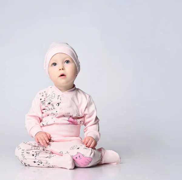 Bebé infante en un cuerpo con mangas largas y un shianishka, un sombrero a juego, con un patrón infantil divertido en su ropa, se sienta en el suelo en el estudio. — Foto de Stock