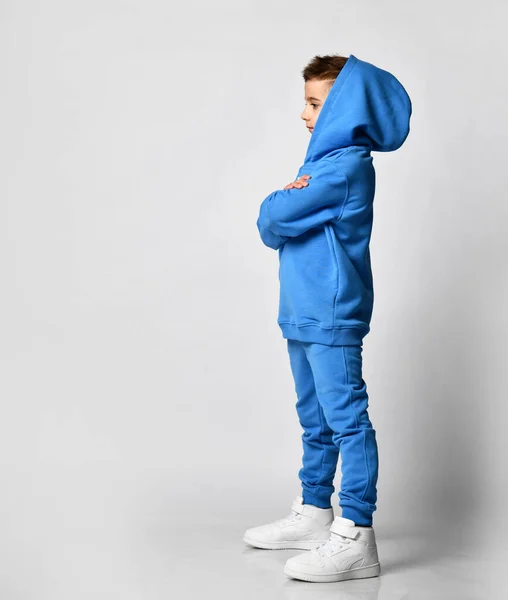 Profil eines kleinen brünetten Jungen in blauer Sportbekleidung und weißen Turnschuhen. — Stockfoto