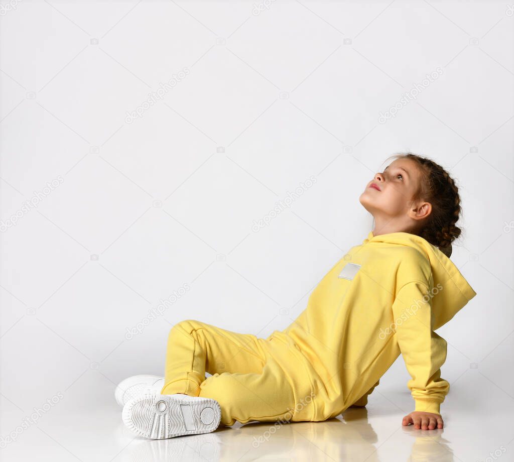 Stylish little girl sitting on a white background and dreamily looking up.