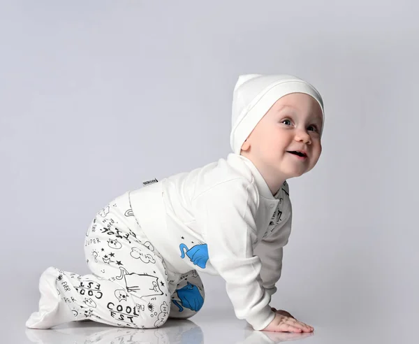 Side view of a satisfied creeping 10 month old baby in bright body and pantish, in a cute hat. — Stock Photo, Image