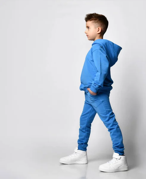 Ritratto a figura intera di un ragazzo con un taglio di capelli elegante in moderne tonalità pastello di blu con cappuccio e pantaloni, in piedi lateralmente davanti alla fotocamera — Foto Stock