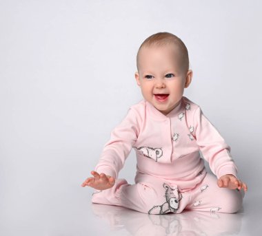 Stüdyoda, pamuklu bir takım elbiseyle, hafif arka planda, yerde oturan sevimli bir bebek. izole