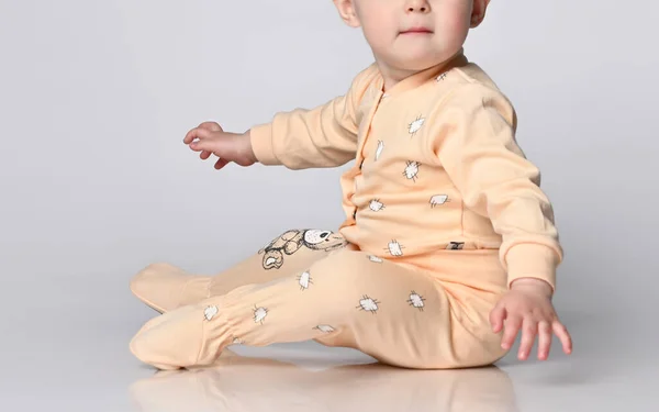 Faceless little toddler toddler child sits on the floor in the studio in a cotton yellow jumpsuit for baby — Stock Photo, Image