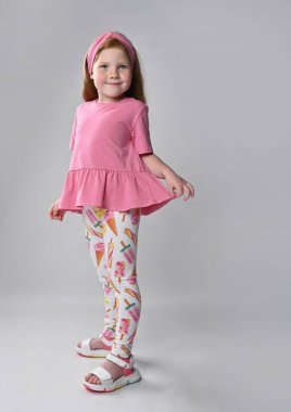 Düşünceli küçük kızıl saçlı kız çocuğu yaz modasını gösteriyor.