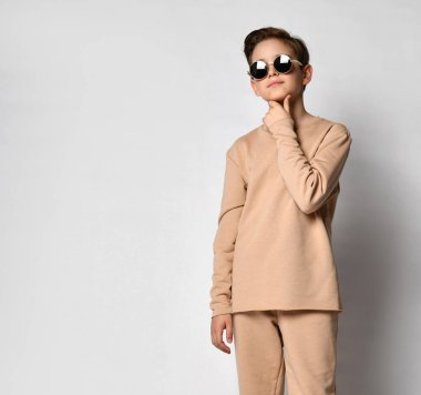 Bej renkli Gordian marka rahat takım elbiseli, kazaklı, bronz tenli, elleri önünde katlanmış, güneş gözlüğü takan mütevazı bir adam.