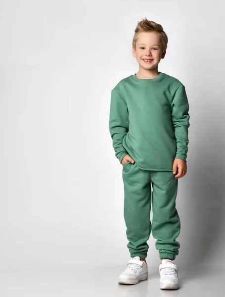 Lindo niño activo en los deportes de moda ropa verde de pie con la mano en el bolsillo mostrando emociones de felicidad y comodidad. — Foto de Stock