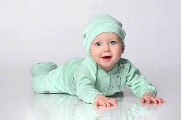 小婴儿蹒跚学步，头戴一套滑翔机和帽子，爬在白色背景的地板上. — 图库照片