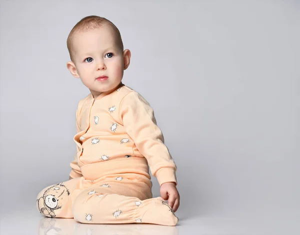Pequeño bebé lindo sentado en el suelo en el estudio en un traje de algodón de verano, en un traje de algodón sobre un fondo claro. aislado —  Fotos de Stock