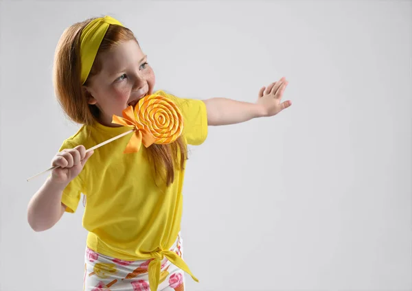 Lachend klein roodharig meisje likken lolly 's zijaanzicht studio schot — Stockfoto