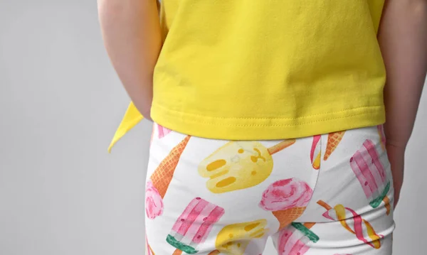 Vista trasera de un detalle de armario de verano para niños - una camiseta de algodón amarillo con una manga corta y leyendas coloridas —  Fotos de Stock