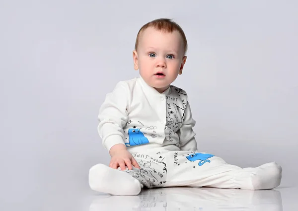 Little cute baby sitting on the floor in the studio in a summer cotton suit, in a cotton suit on a light background. isolated — Stock Photo, Image