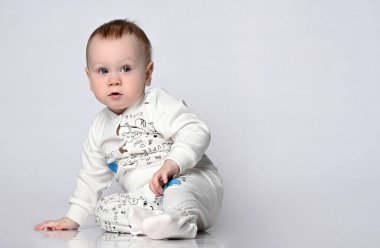 Stüdyoda, pamuklu bir takım elbiseyle, hafif arka planda, yerde oturan sevimli bir bebek. izole