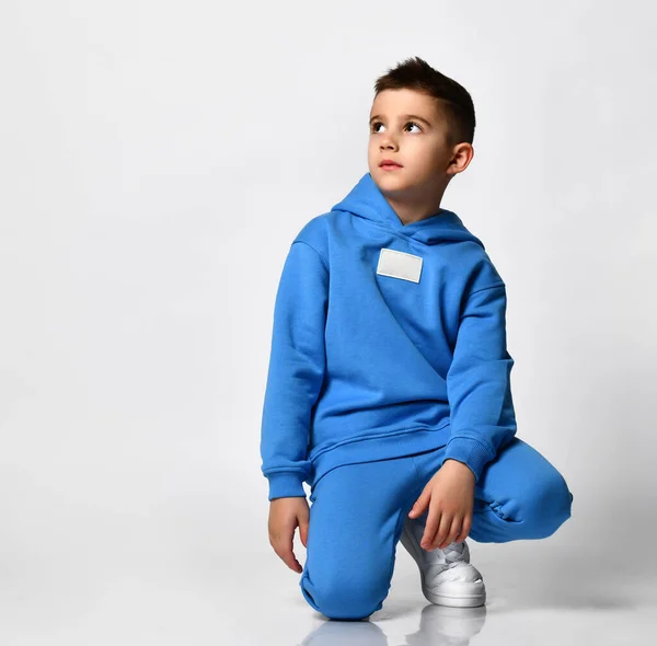 Parlak mavi spor kıyafetleriyle beyaz arka planda oturan havalı okul çocuğu.. — Stok fotoğraf