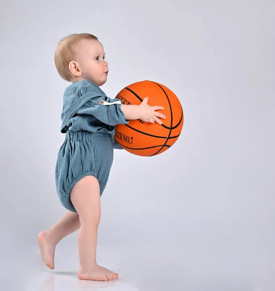 Ένα μικρό παιδί κρατά ένα μεγάλο πορτοκαλί μπάσκετ μπροστά του.. — Φωτογραφία Αρχείου