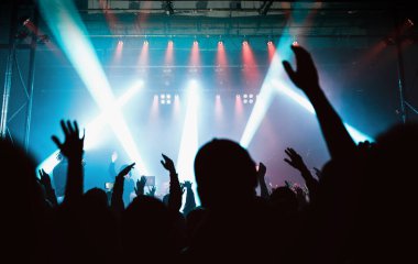 Bir müzik festivalinde elleri havada seyirciler ve sahneden ışıklar yükseliyor..