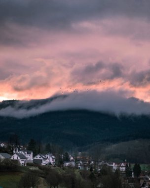 Almanya 'da küçük bir kasabada gün batımının güzel manzarası. Arka planda büyük dağlar var. Sis ve bulutlar dağın zirvesini gizliyor. Schwarzwald doğası