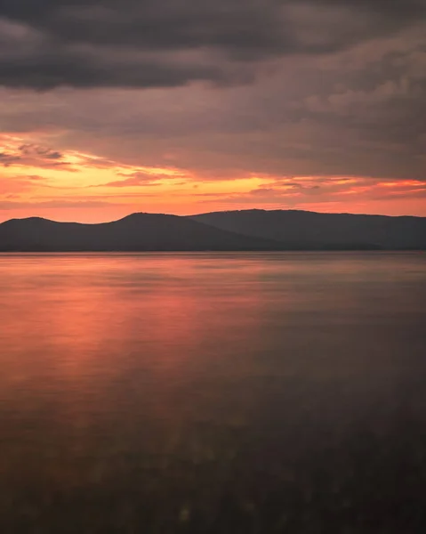 Photography of the sunset on the sea. Orange reflection on the water, mountains in the background. Dramatic view, breathtaking seascape. Golden sun rays.