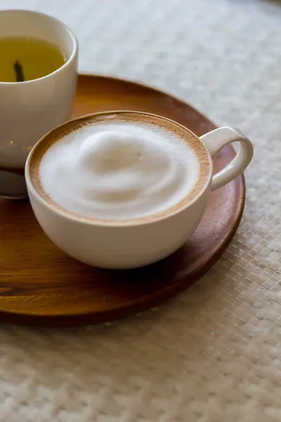 Cappuccino in a white cup on a white plate on wood table — Stock Photo, Image