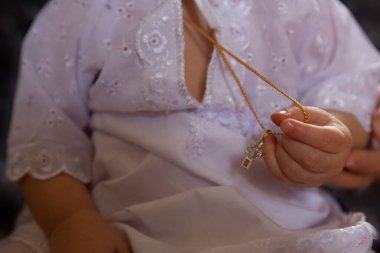 Epifani ziyafeti: beyaz vaftizli bir çocuk küçük bir el ile boynunda bir iple bir haç tutuyor.