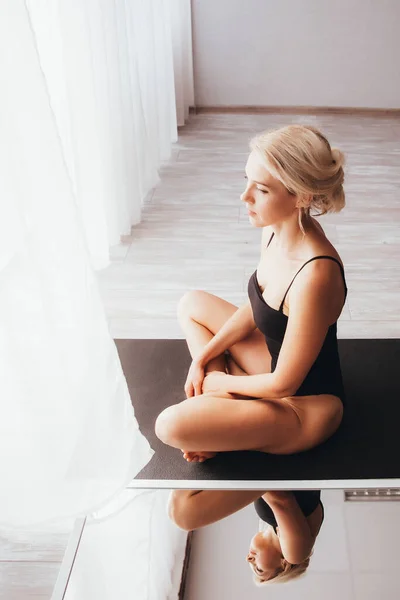 一个穿着运动服的金发美女在镜子前的垫子上做瑜伽和冥想 — 图库照片