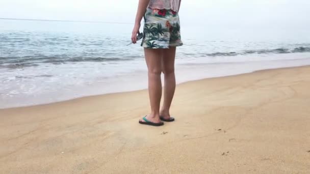 En kvinna med sandaler gick längs stranden och lämnade fotspår i sanden. De sköljdes av havets vågor. Begreppet marin avkoppling — Stockvideo