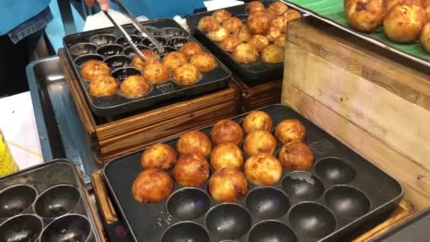 Chef hand pick up Japanese snack food takoyaki from takoyaki pan into the box for selling in summer festival at street food market in Japan. Man cooking assorted traditional Japanese meat ball. — Stock Video