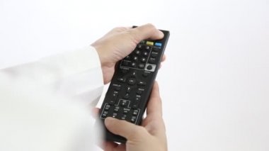 Televizyonun uzaktan kumandası, televizyonu gösteren ve kanalı değiştiren kadının elinde. Kadın kumandayı tutarken ve televizyon karşısında koltukta otururken düğmeye basarken..