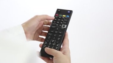 Televizyonun uzaktan kumandası, televizyonu gösteren ve kanalı değiştiren kadının elinde. Kadın kumandayı tutarken ve televizyon karşısında koltukta otururken düğmeye basarken..