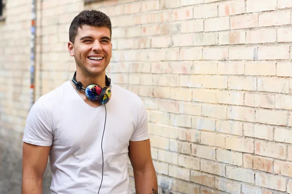 Jonge man in stedelijke achtergrond muziek met een hoofdtelefoon beluisteren — Stockfoto