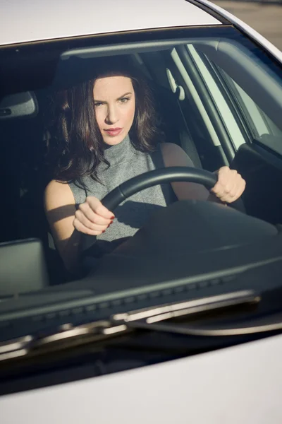 Brunette woman driving a white car in urban background — Stock Photo, Image