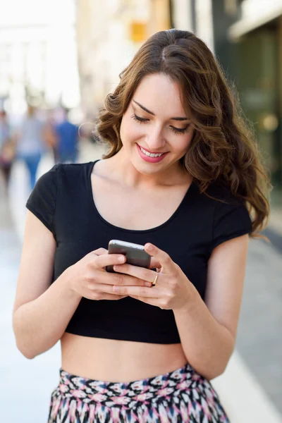 Giovane donna sms con uno smartphone in background urbano — Foto Stock