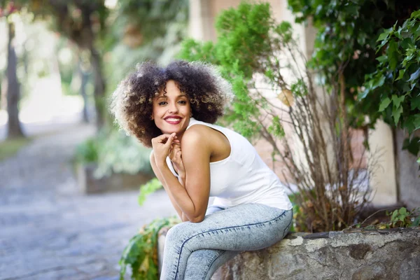 Jonge zwarte vrouw met afro kapsel glimlachend in stadspark — Stockfoto