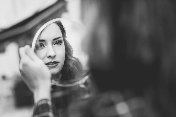 Junge Frau sieht sich selbst in einem kleinen Spiegel an — Stockfoto
