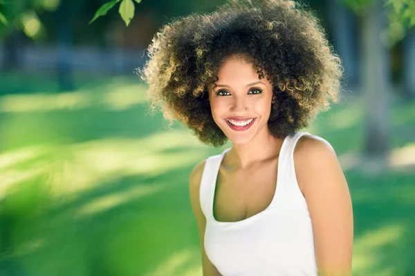 Jonge zwarte vrouw met afro kapsel glimlachend in stadspark — Stockfoto