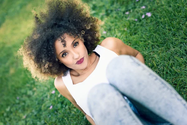 Jeune femme noire avec coiffure afro assis dans un parc urbain — Photo