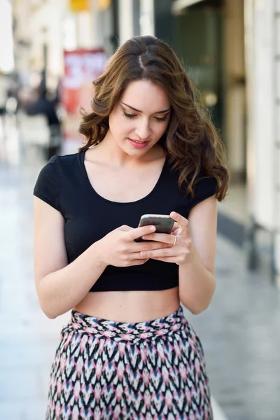 Giovane donna sms con uno smartphone in background urbano — Foto Stock