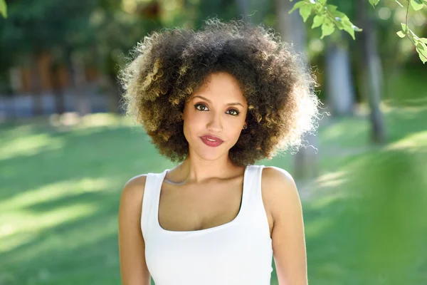 Jonge zwarte vrouw met afro kapsel glimlachend in stadspark — Stockfoto