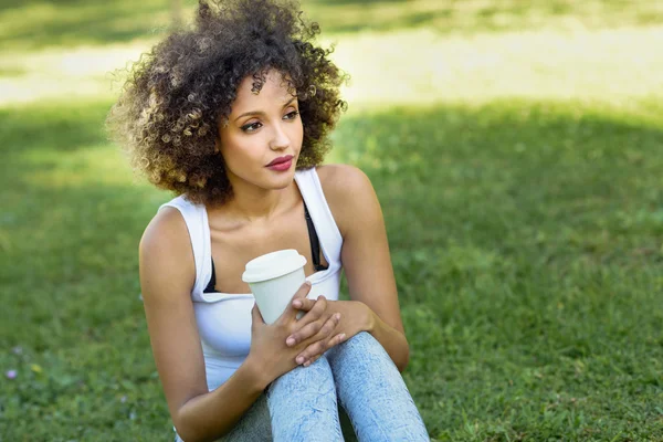 Donna con acconciatura afro bere caffè nel parco — Foto Stock