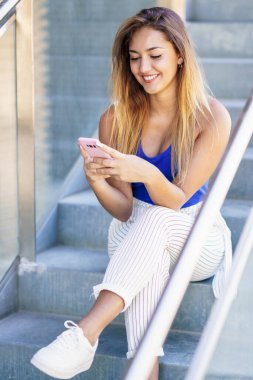 Dokunmatik ekranlı akıllı telefon kullanan ve günlük kıyafetler giyen bir kız.