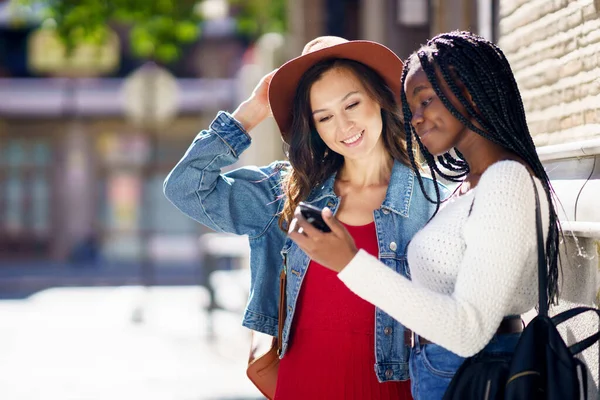 Dos amigos mirando su smartphone juntos. Mujeres multiétnicas. — Foto de Stock