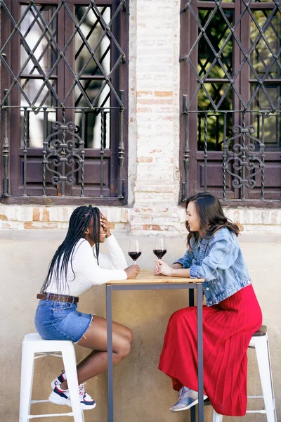 Dos mujeres bebiendo vino tinto sentadas en una mesa fuera de un bar. —  Fotos de Stock