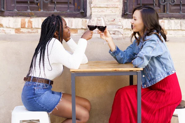 Duas mulheres fazendo um brinde com vinho tinto sentado em uma mesa do lado de fora de um bar. — Fotografia de Stock